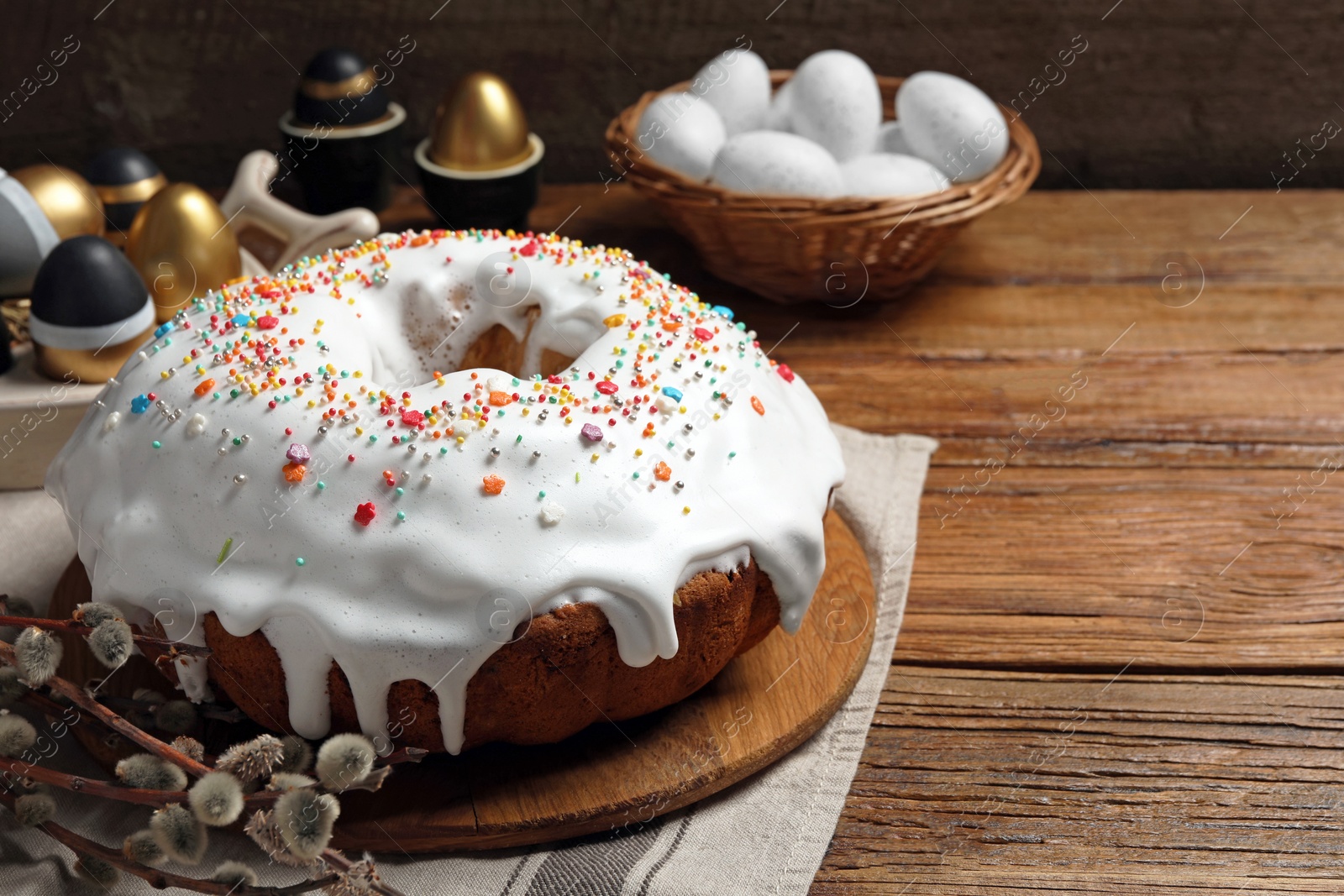 Photo of Delicious Easter cake decorated with sprinkles near painted eggs and willow branches on wooden table. Space for text