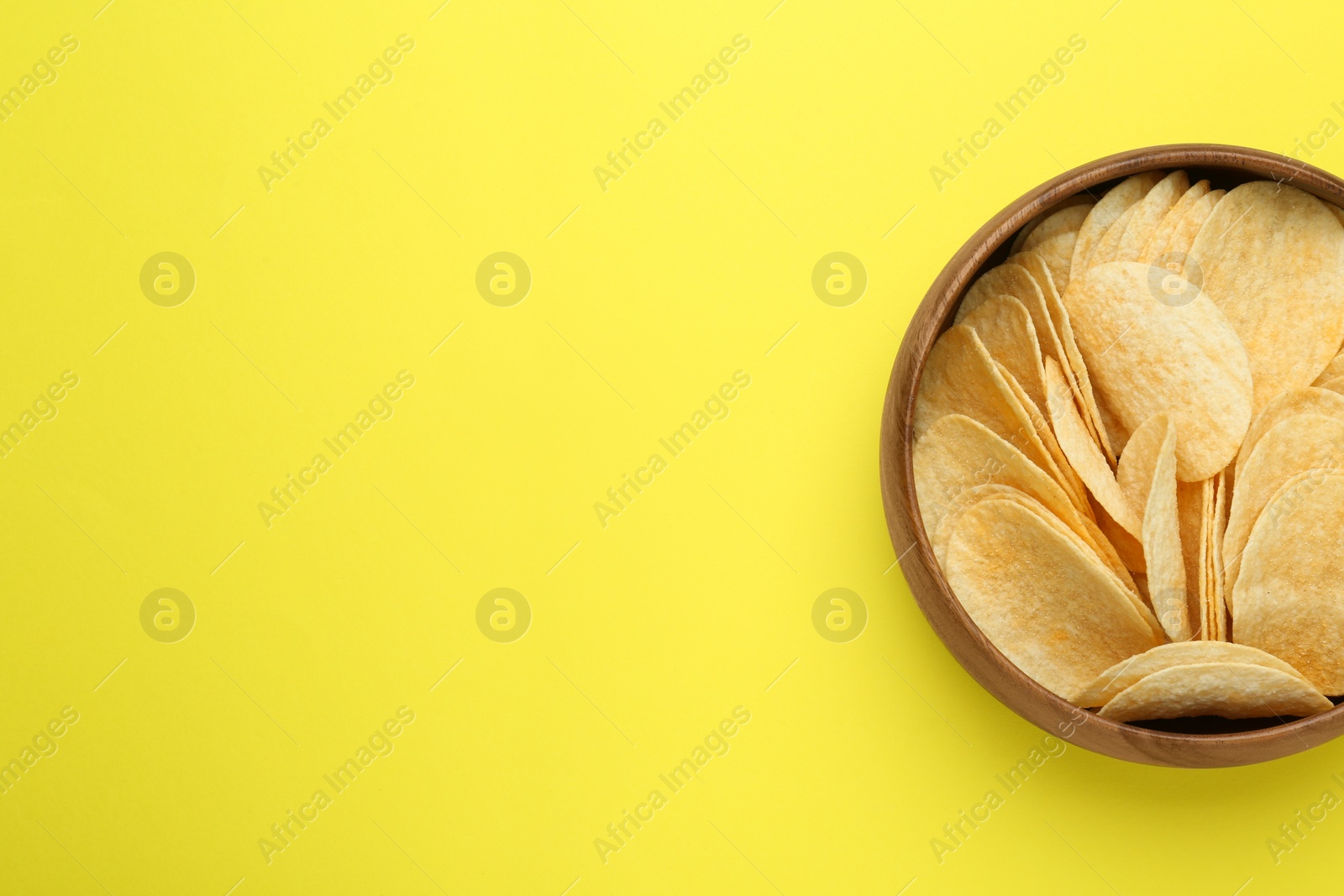 Photo of Bowl of tasty potato chips on yellow background, top view. Space for text