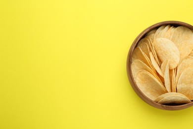 Bowl of tasty potato chips on yellow background, top view. Space for text