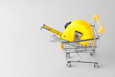 Photo of Metal wrench and measuring tape in shopping cart on light grey background, space for text