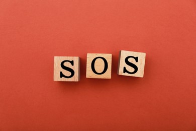Abbreviation SOS made of wooden cubes on red background, top view