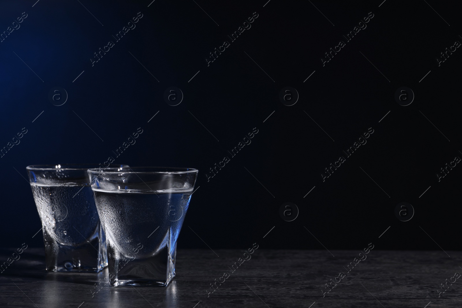 Photo of Vodka in shot glasses on black table against dark background. Space for text