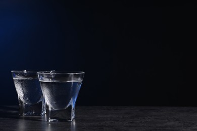 Photo of Vodka in shot glasses on black table against dark background. Space for text