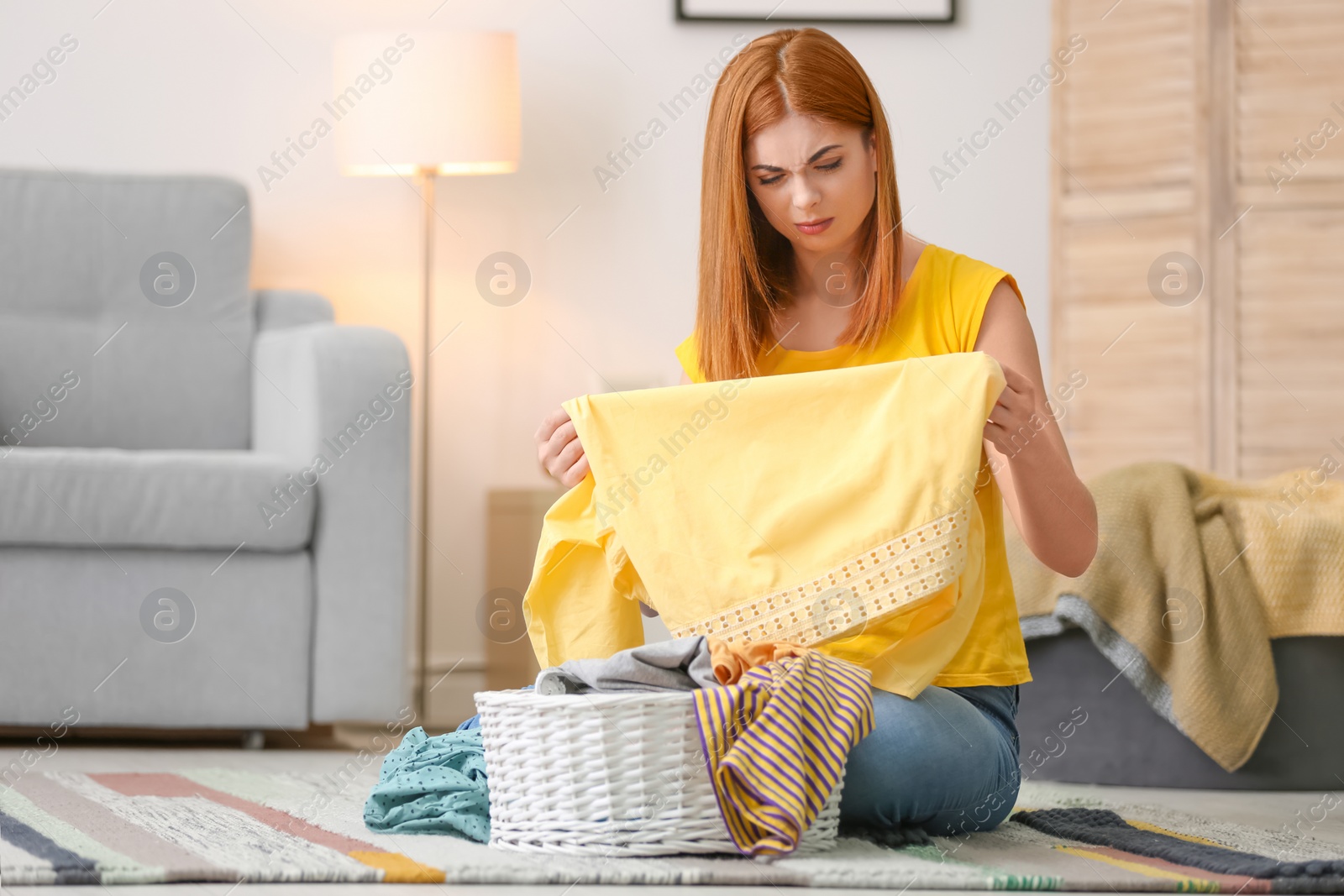 Photo of Tired housewife with laundry sitting on floor at home