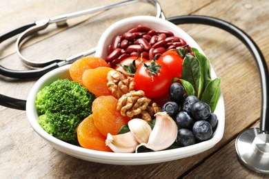 Photo of Bowl with products for heart-healthy diet and stethoscope on wooden table