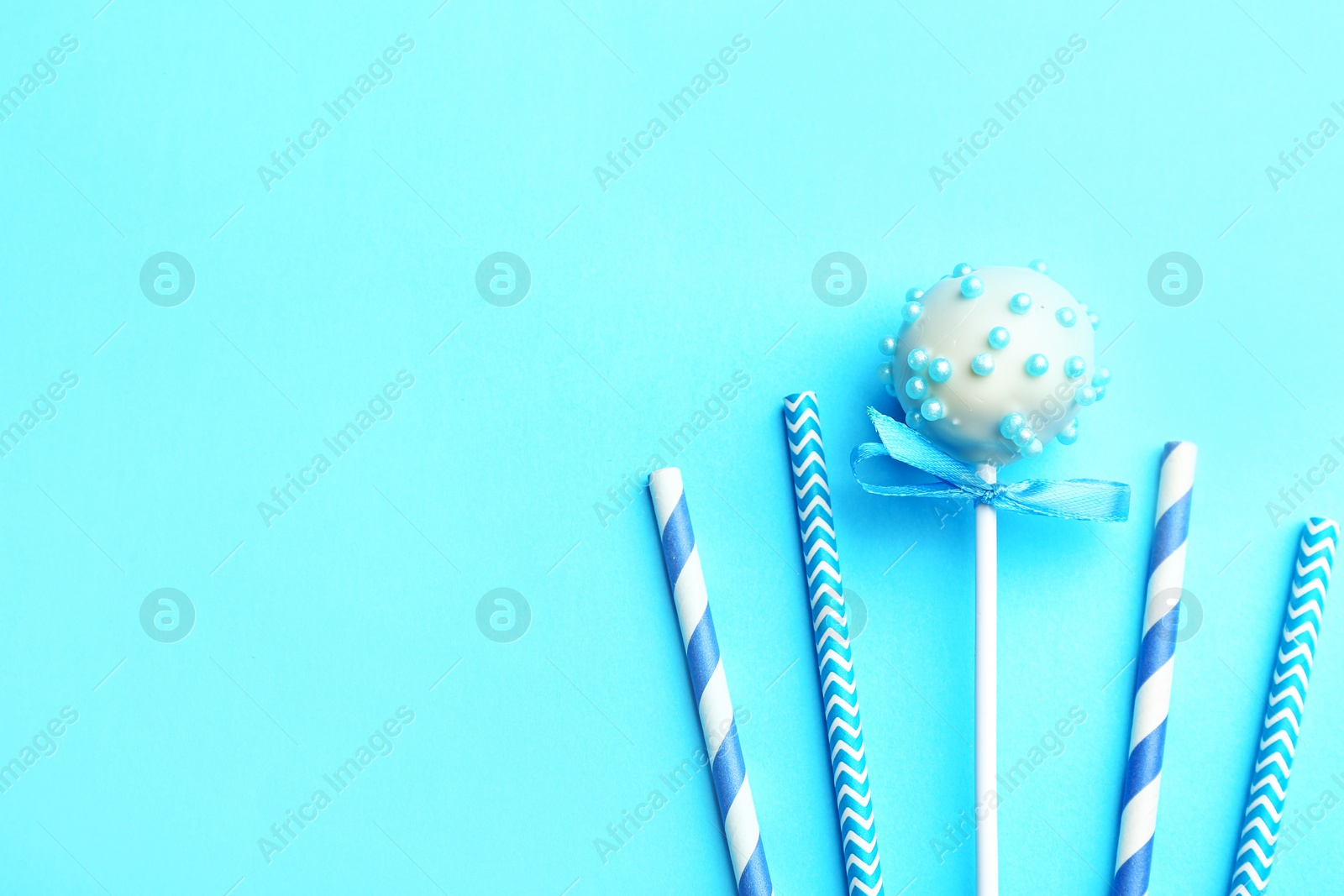 Photo of Tasty cake pop and straws on light blue background, flat lay. Space for text