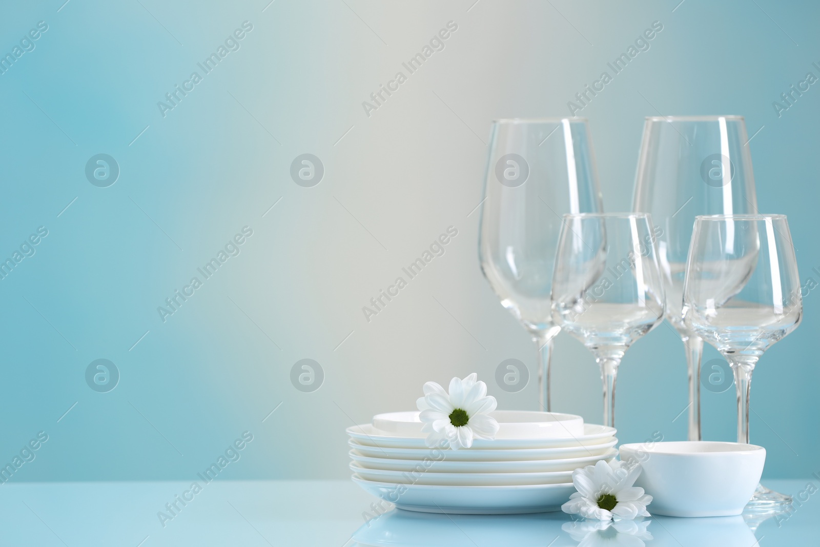 Photo of Set of many clean dishware, flowers and glasses on light blue table. Space for text