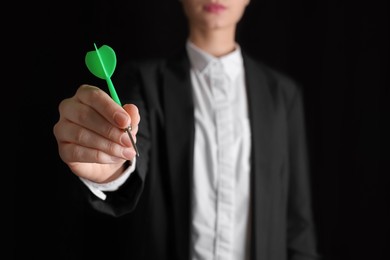 Businesswoman holding green dart on black background, closeup