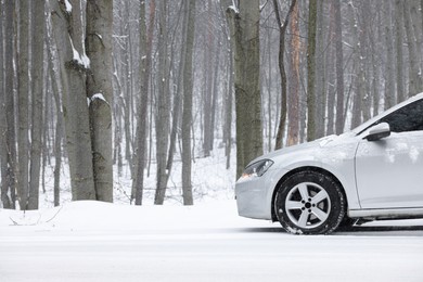 Car with winter tires on snowy road in forest, space for text