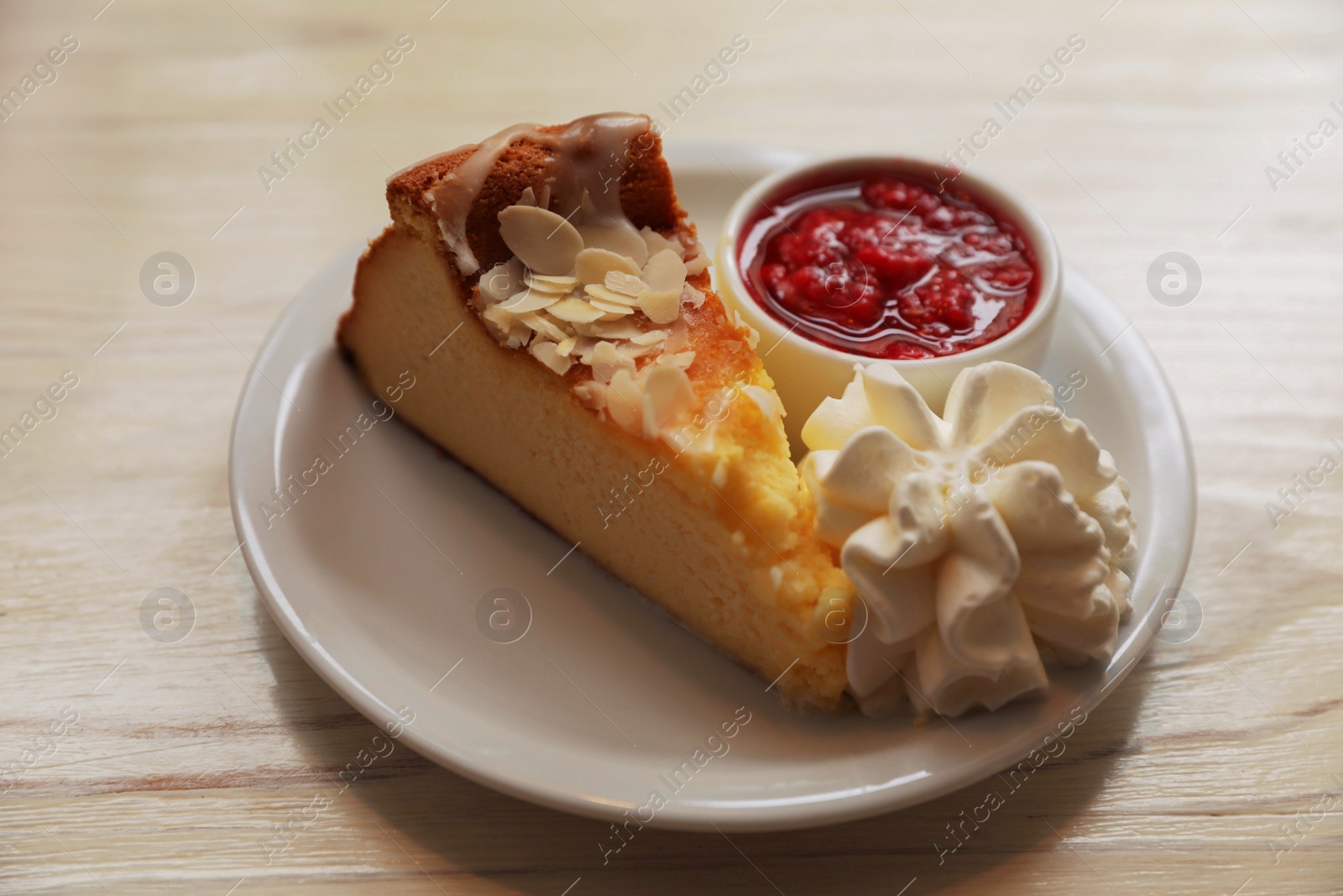 Photo of Piece of delicious cake with whipped cream and jam on white wooden table, closeup