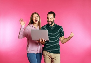 Emotional young people with laptop celebrating victory on color background