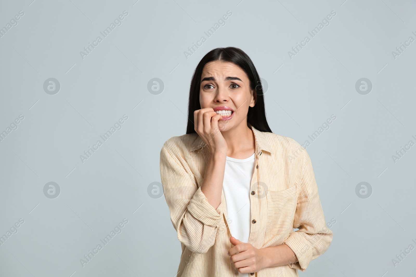 Photo of Young woman biting her nails on light grey background. Space for text