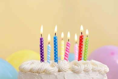 Delicious cake with burning candles and festive decor on yellow background, closeup