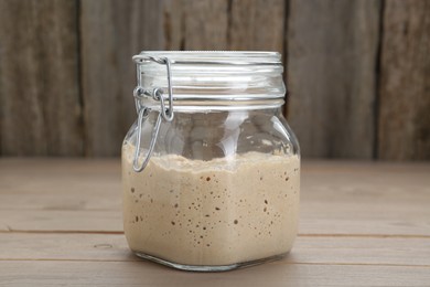Photo of Leaven in glass jar on beige wooden table