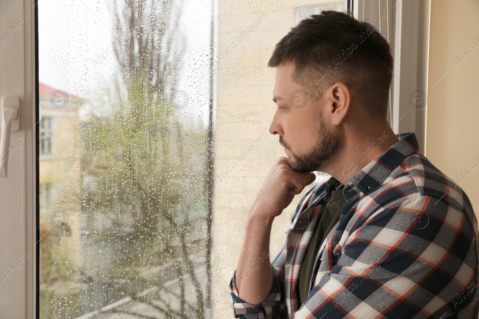 Photo of Depressed man near window at home. Space for text