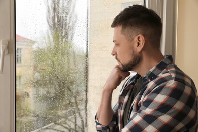 Photo of Depressed man near window at home. Space for text