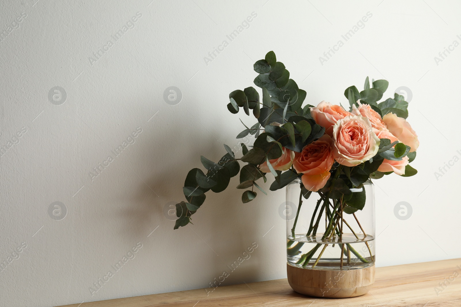 Photo of Bouquet with beautiful flowers in glass vase on wooden table against white background. Space for text