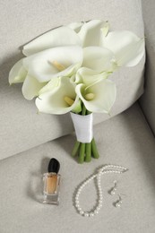 Photo of Beautiful calla lily flowers tied with ribbon, bottle of perfume and jewelry on sofa