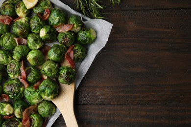 Photo of Delicious roasted Brussels sprouts, bacon, rosemary and spatula on wooden table, top view. Space for text