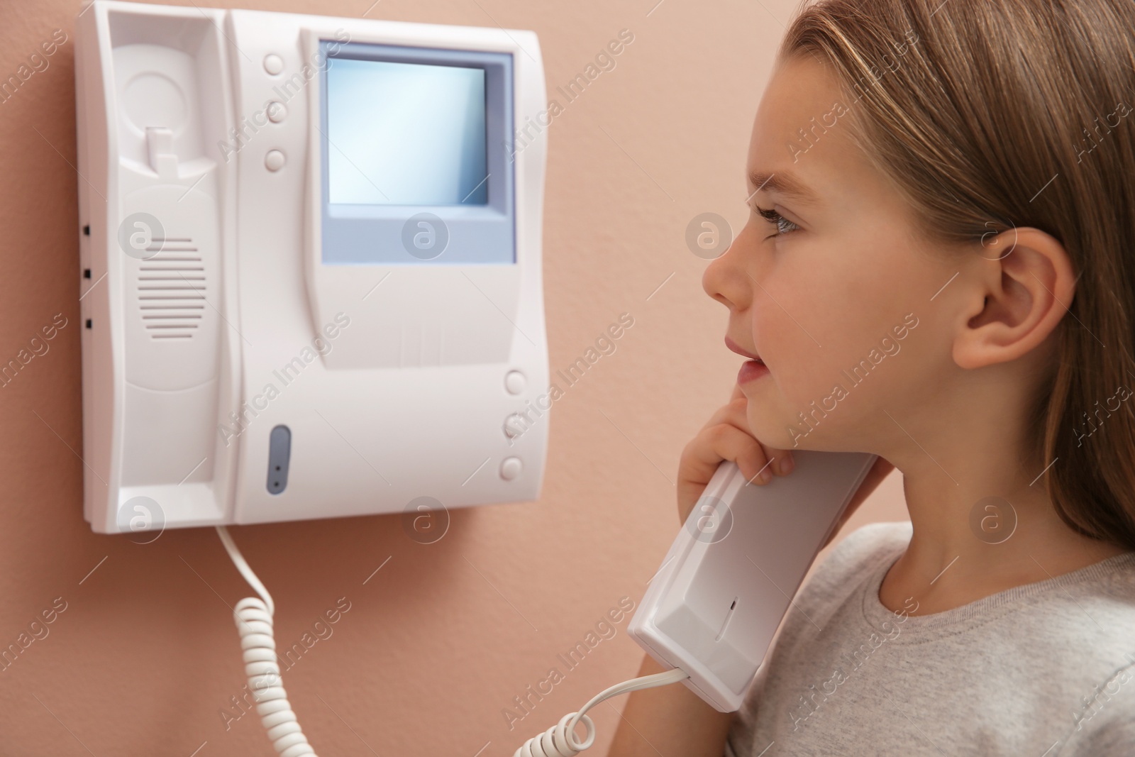 Photo of Cute little girl answering intercom call indoors