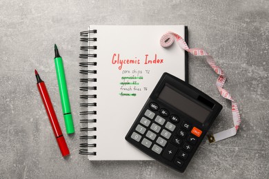 Photo of Glycemic Index. Notebook with information, markers, calculator and measuring tape on light grey table, flat lay