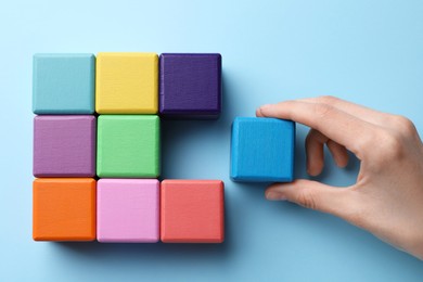 Photo of Woman with colorful cubes on light blue background, top view. Management concept