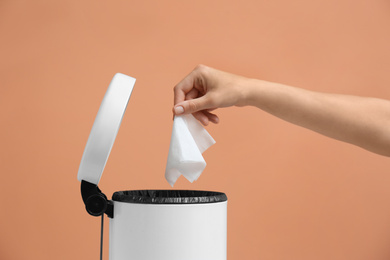 Photo of Woman putting paper tissue into trash bin on light brown background, closeup