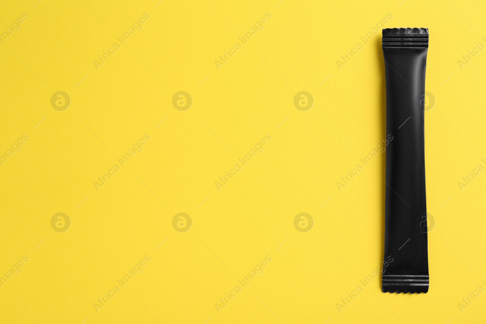 Photo of Black stick of sugar on yellow background, top view. Space for text
