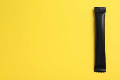 Black stick of sugar on yellow background, top view. Space for text