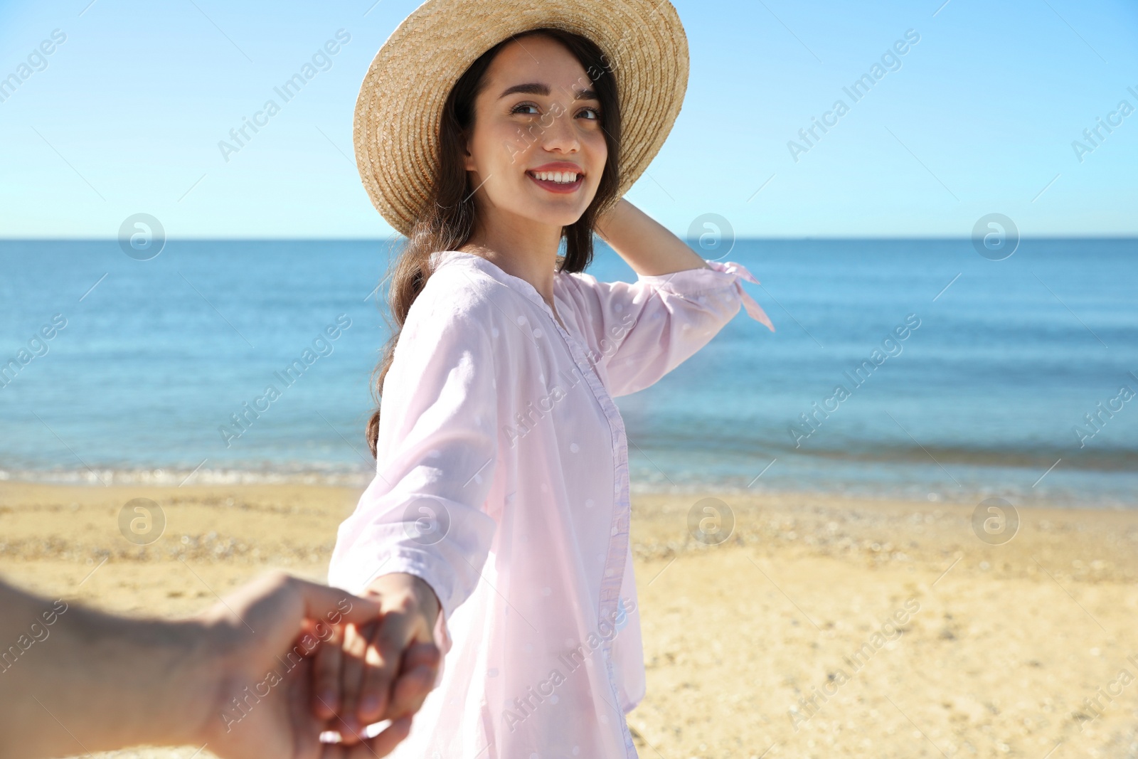 Photo of Happy young woman holding her husband's hand on beach near sea, closeup. Honeymoon trip