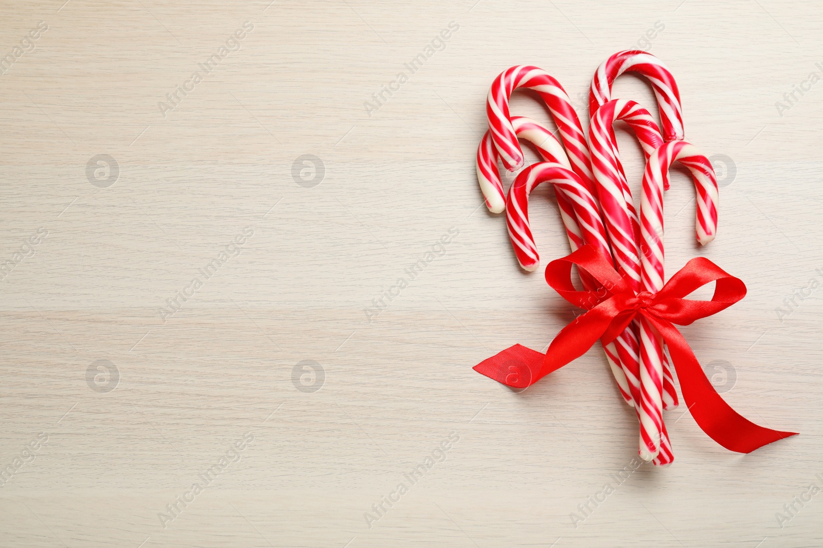 Photo of Sweet Christmas candy canes with red bow on wooden background, top view. Space for text