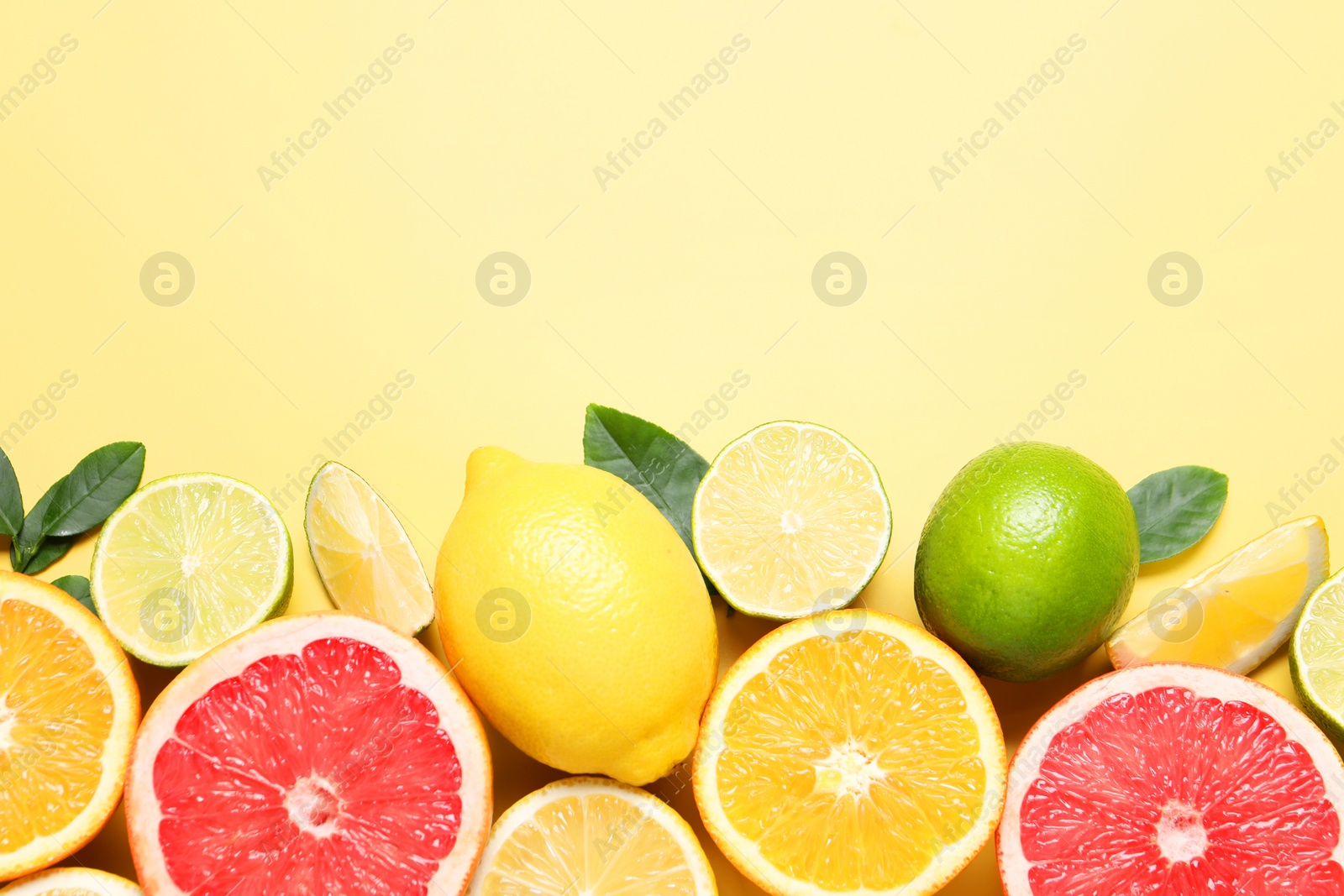 Photo of Different cut and whole citrus fruits on yellow table, flat lay. Space for text