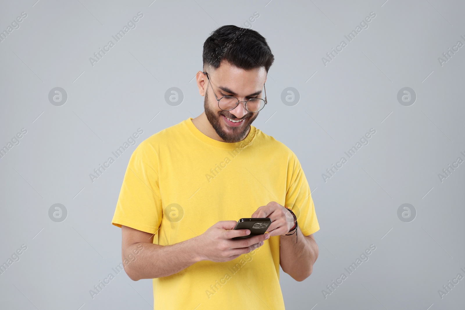 Photo of Happy young man using smartphone on grey background