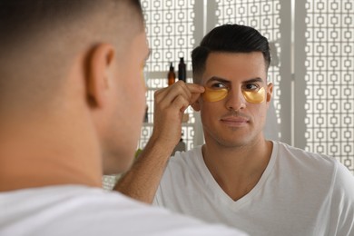Photo of Man applying golden under eye patch near mirror at home