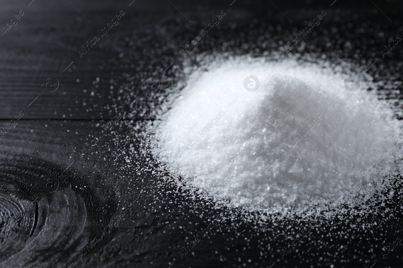 Photo of Pile of organic salt on black wooden table, closeup. Space for text