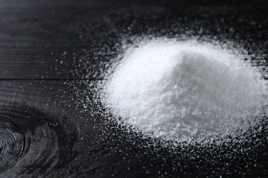 Photo of Pile of organic salt on black wooden table, closeup. Space for text