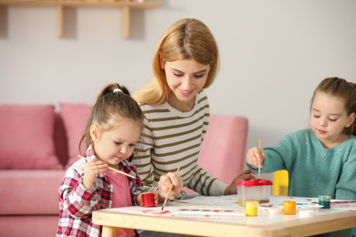 Mother and daughters painting at table indoors. Playing with children