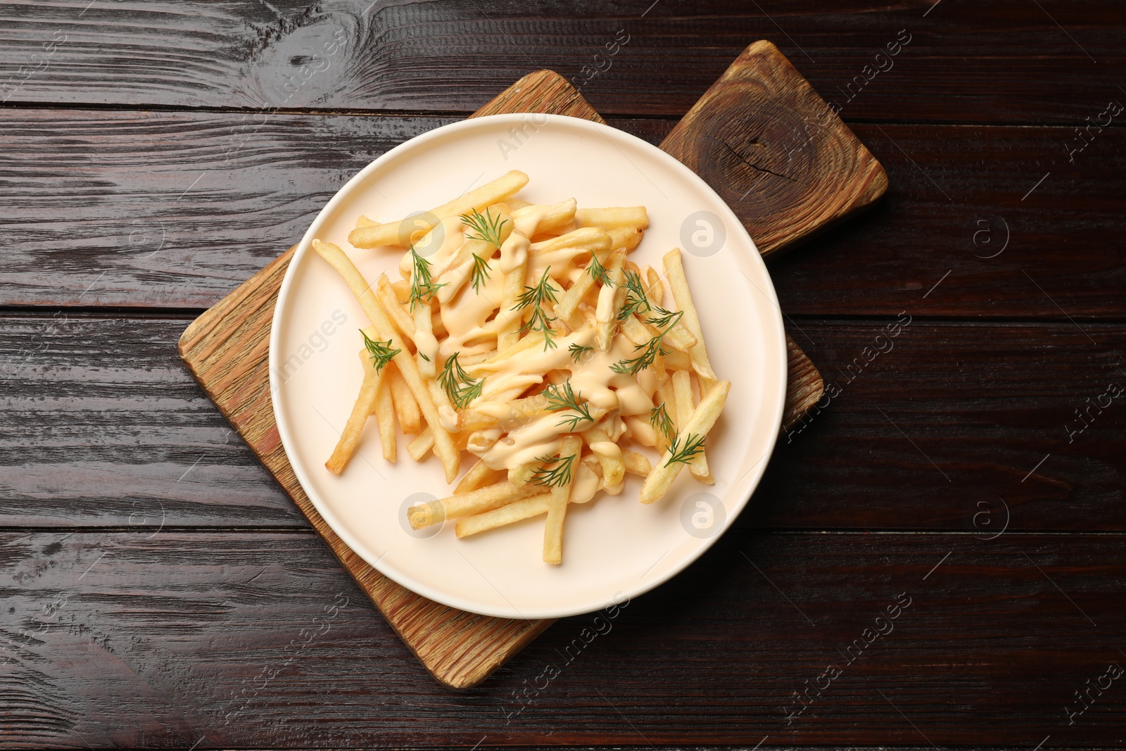 Photo of Delicious french fries with cheese sauce and dill on wooden table, top view