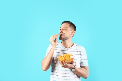 Man eating potato chips on color background