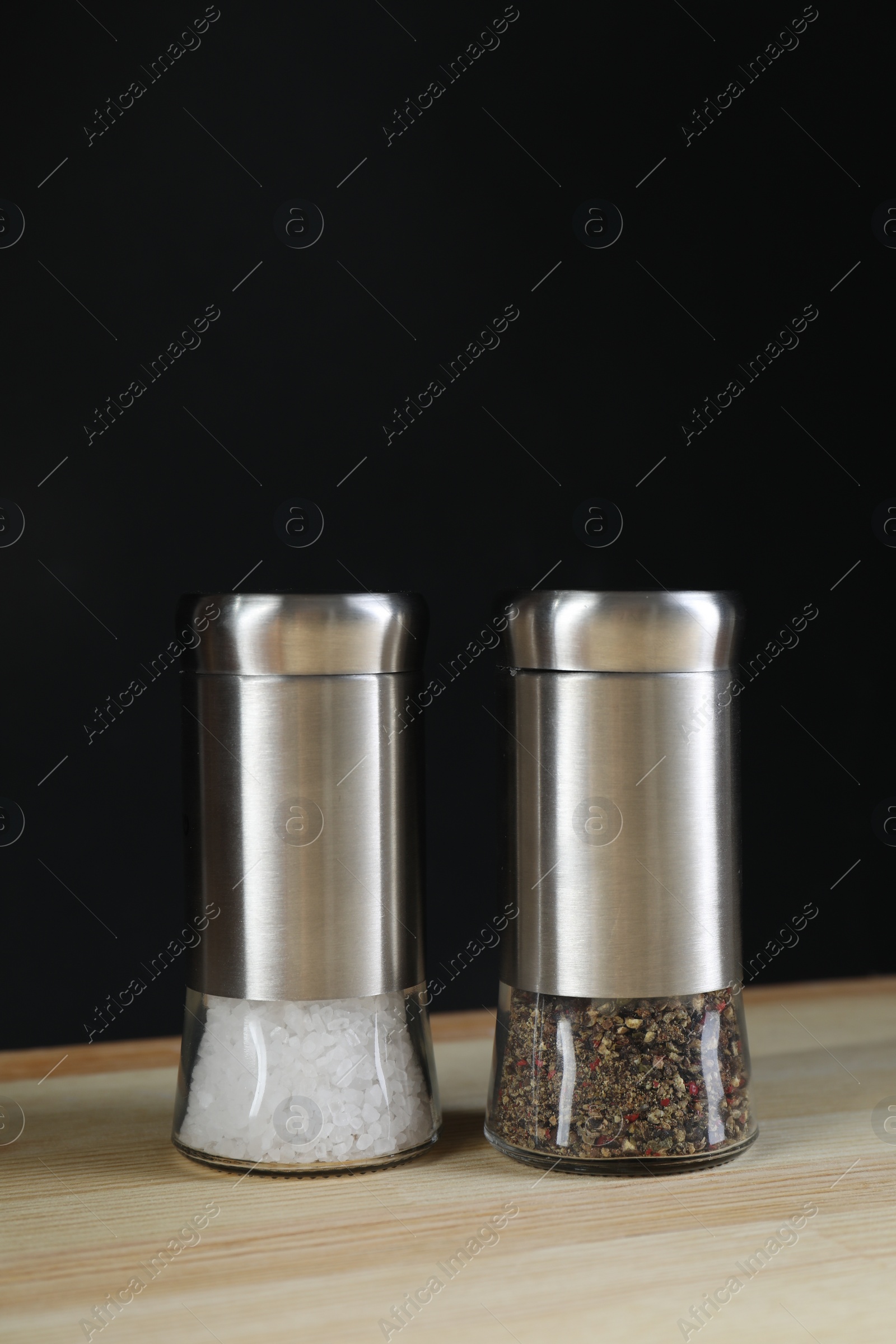 Photo of Salt and pepper shakers on light wooden table against black background. Space for text