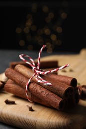 Cinnamon sticks and other spices on table against black background with blurred lights, closeup