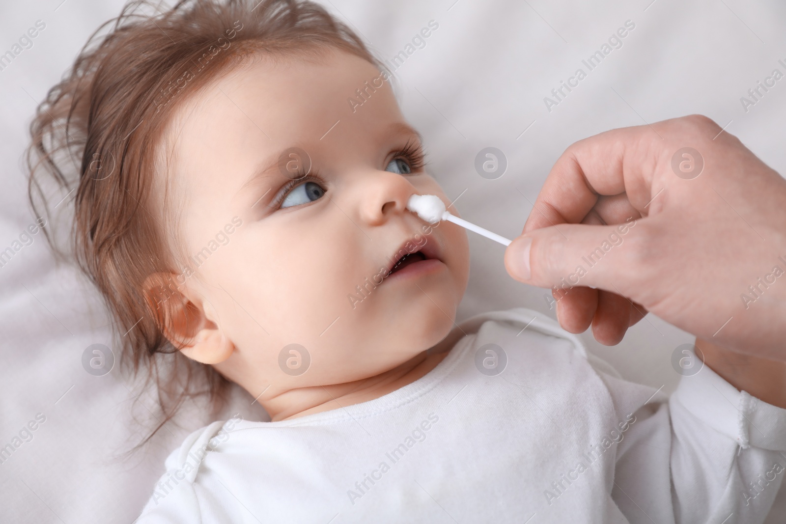 Photo of Father cleaning nose of his baby with cotton bud on bed, closeup