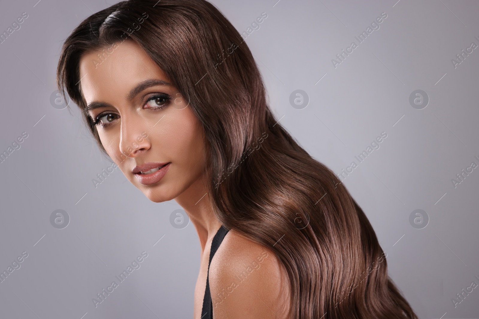 Image of Gorgeous woman with shiny wavy hair on grey background. Professional hairstyling