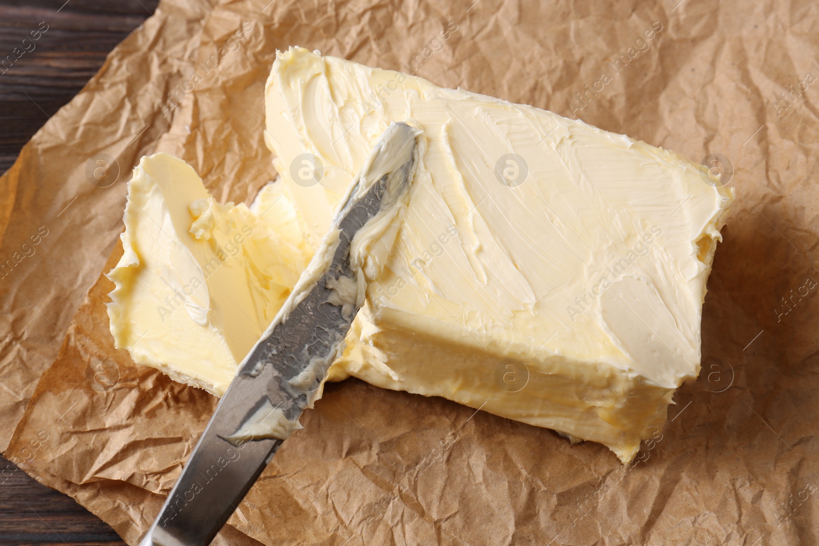 Photo of Tasty homemade butter and knife on parchment, closeup