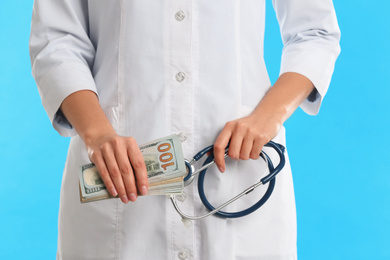Doctor with bribe and stethoscope on light blue background, closeup. Corruption in medicine