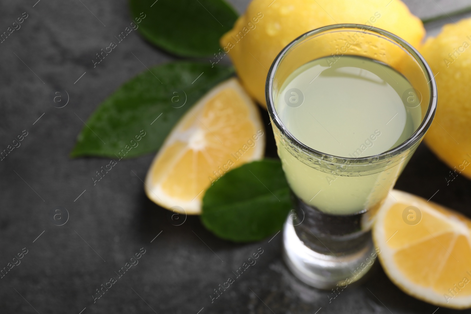 Photo of Tasty limoncello liqueur, lemons and green leaves on grey table, closeup. Space for text
