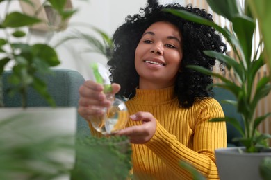 Happy woman spraying beautiful potted houseplants with water indoors