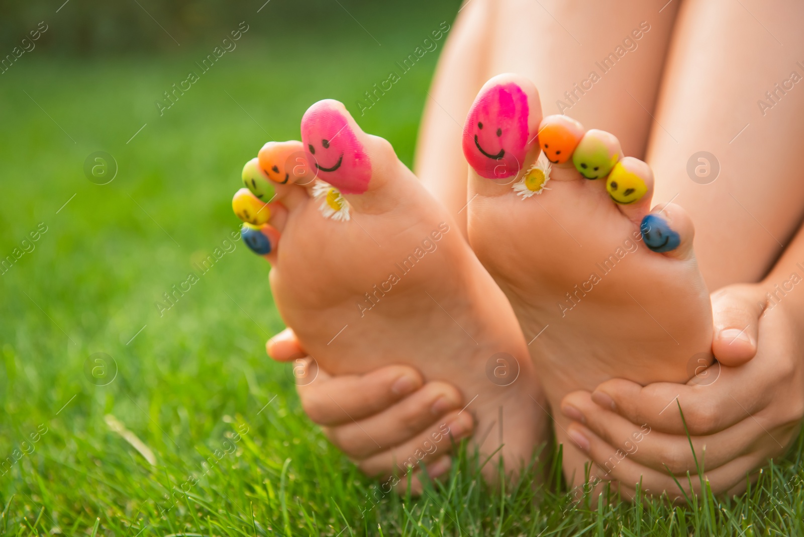 Photo of Teenage girl with chamomiles and smiling faces drawn on toes outdoors, closeup