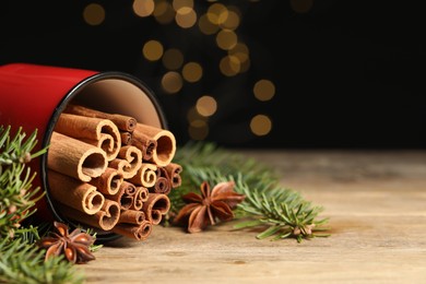 Many cinnamon sticks, anise stars and fir branches on wooden table, closeup. Space for text