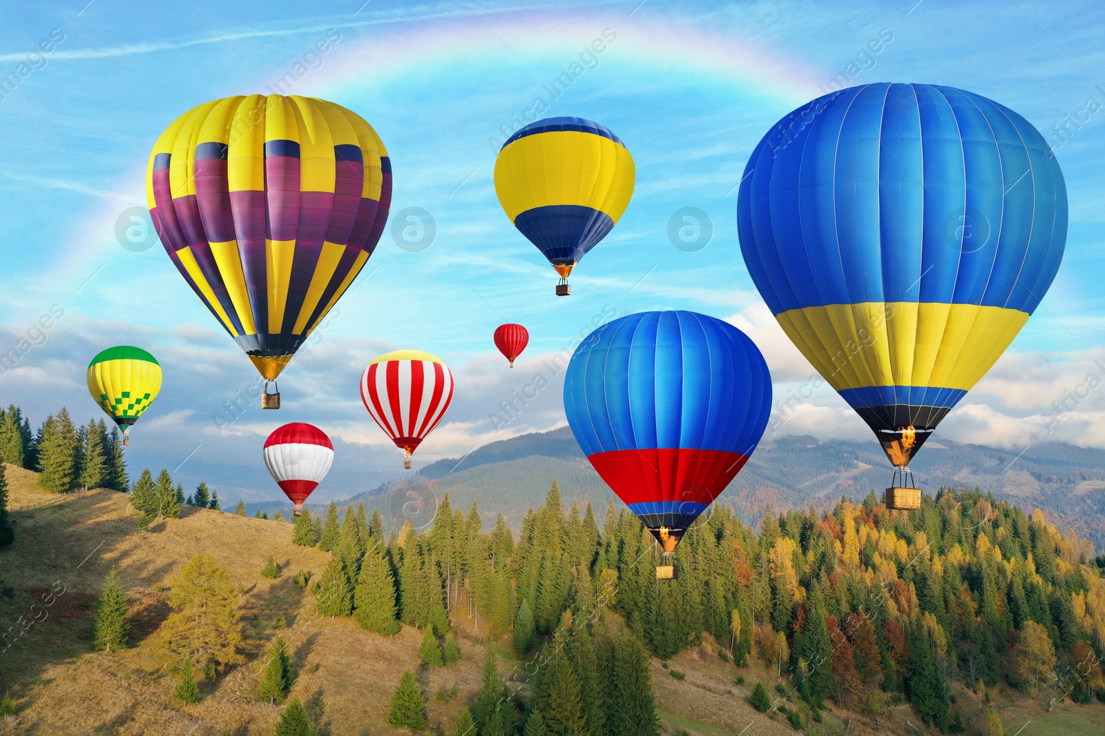 Image of Bright hot air balloons flying in sky with rainbow over mountain